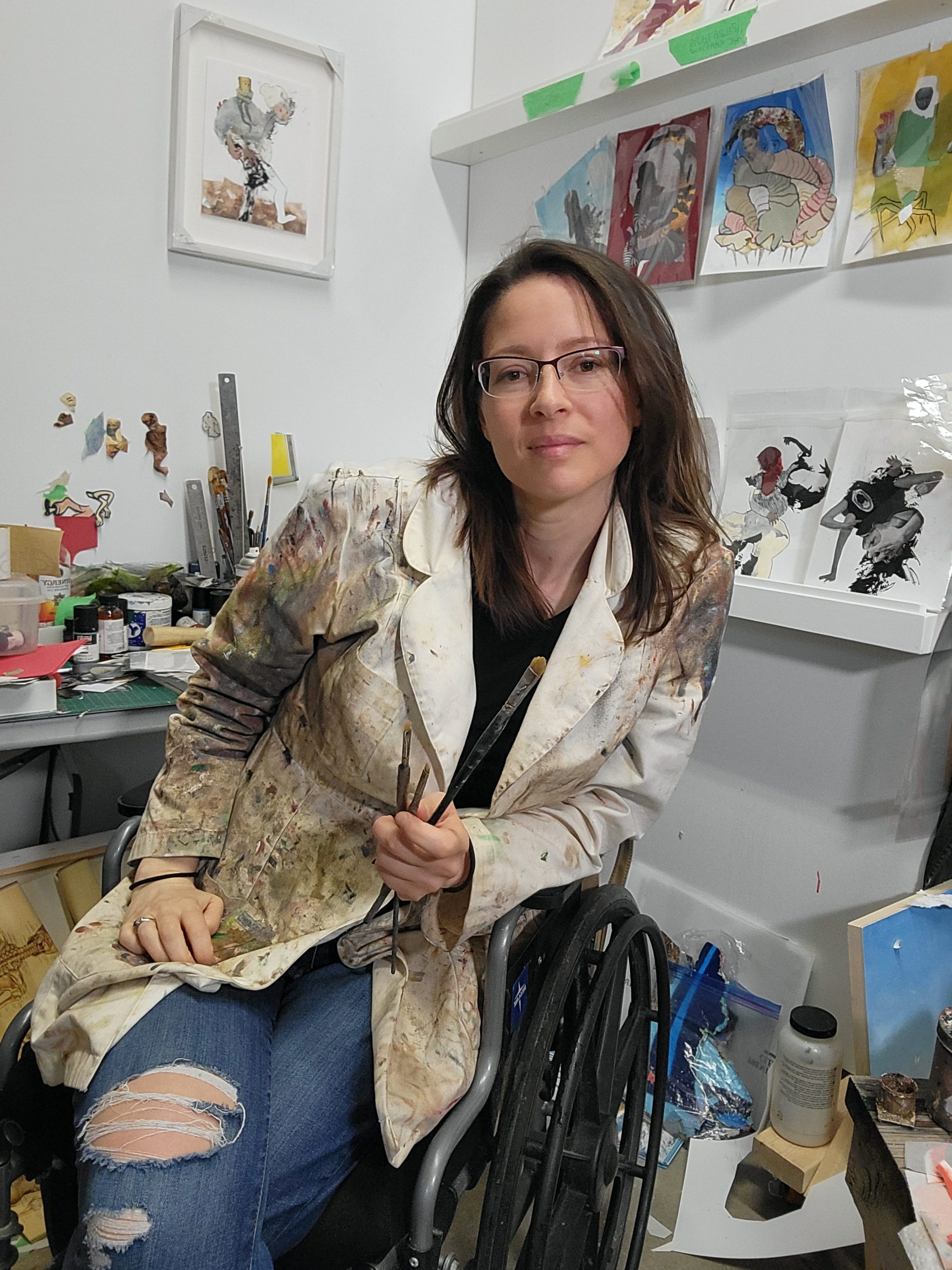 Photo of artist Amy J. Dyck in a wheelchair at her studio holding a paintbrush